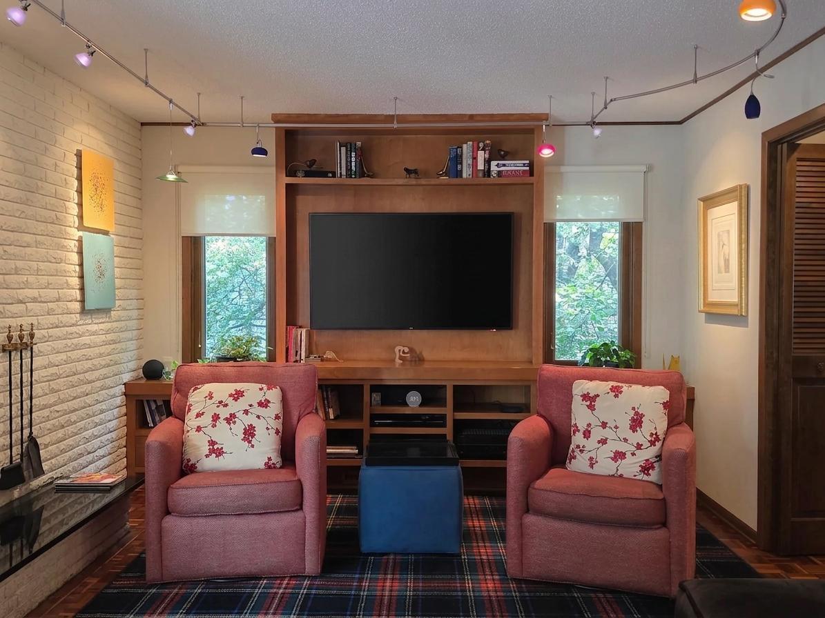 Comfortable family room featuring a custom built-in media center, distinctive track lighting, large windows, and a brick fireplace just steps away.
