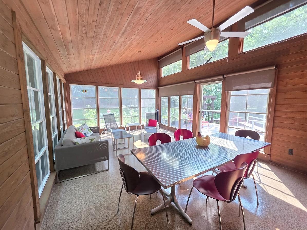 Sun-filled porch with vaulted wood ceiling, walls of collapsible vinyl windows, ceiling fan, and plenty of space for both dining and relaxing.