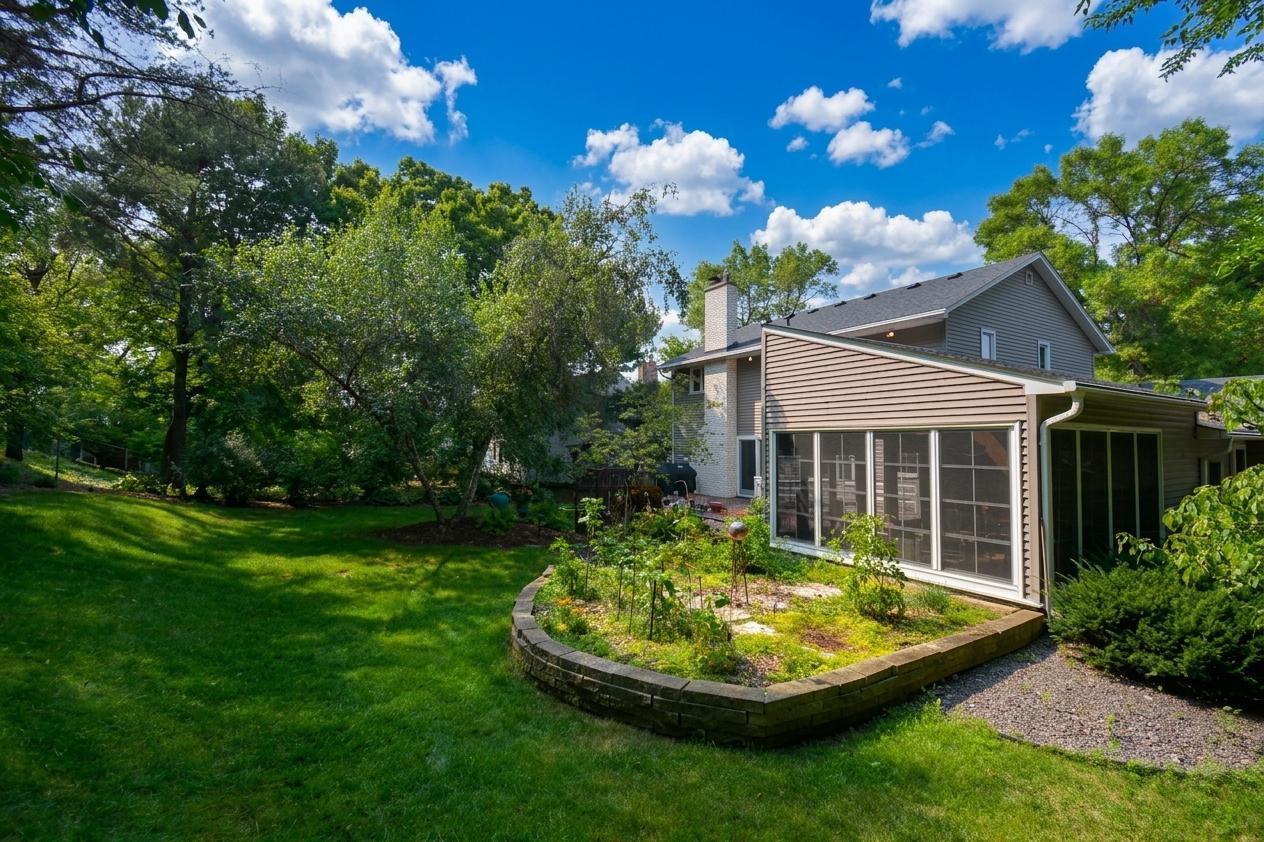 Private backyard setting surrounded by mature trees, lush lawn, established landscaping, and a bright three-season porch overlooking the grounds.