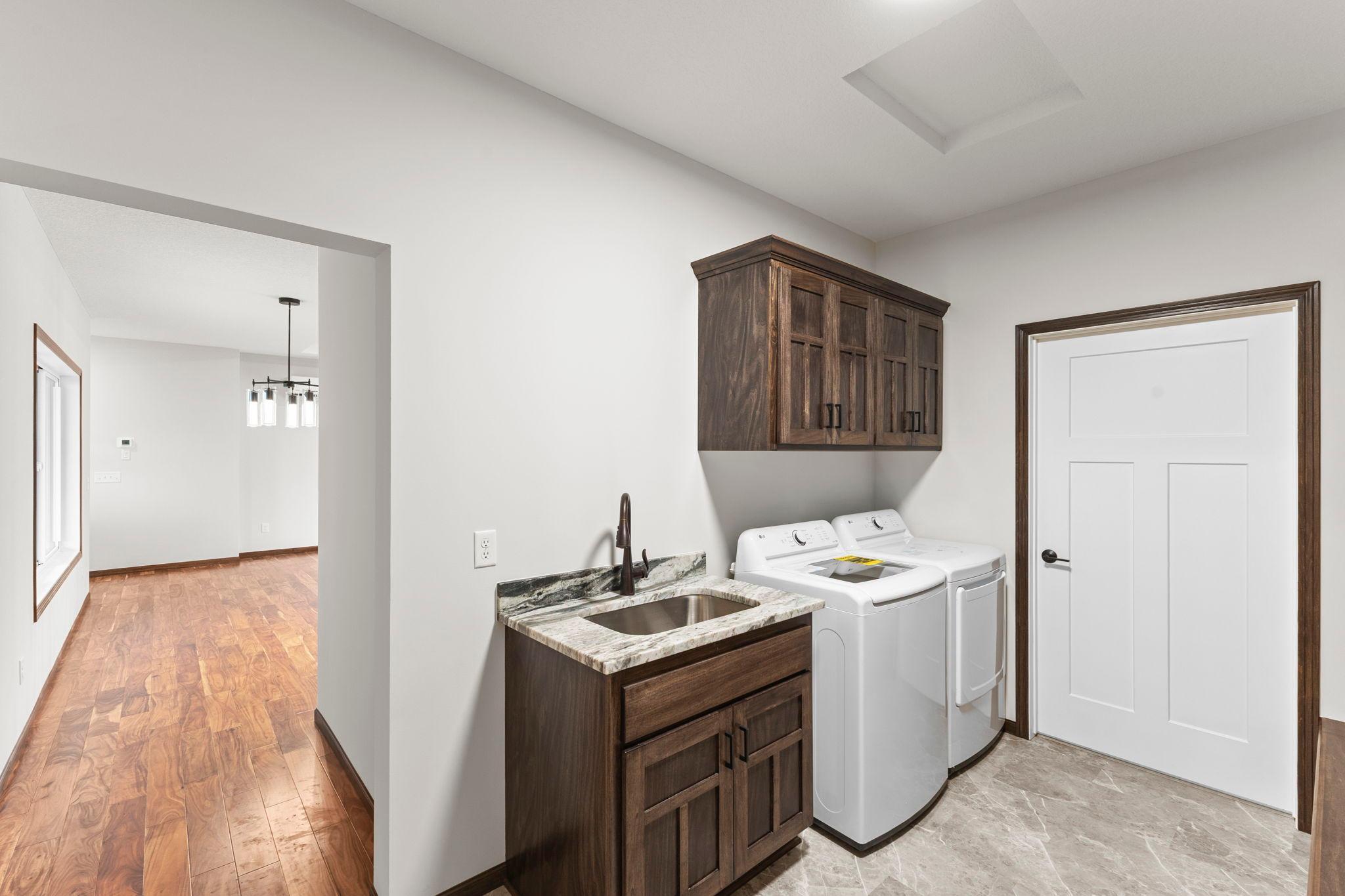 Spacious laundry area with custom cabinetry, granite countertop, and utility sink