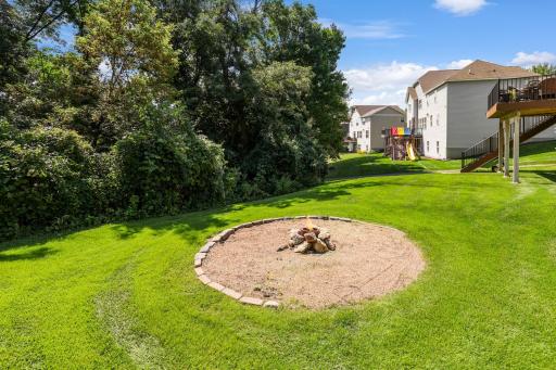 Close-up of the built-in fire pit area bordered by mature trees and lush woods along the lot line, offering exceptional privacy and a cozy outdoor setting.