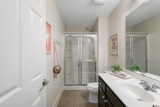A convenient attached bathroom featuring a dark wood vanity with ample storage, and a standalone glass door walk-in shower.