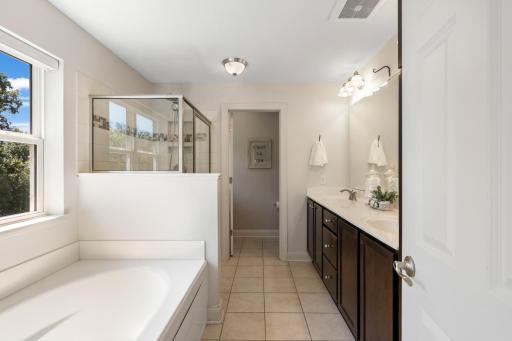 Deluxe primary bathroom equipped with a double vanity featuring rich dark cabinetry, a glass-enclosed walk-in shower with tile detail, a deep soaking tub, and a separate private water closet.
