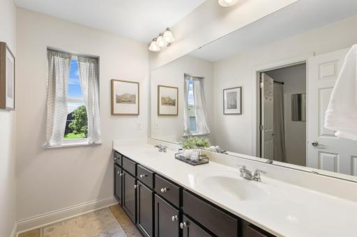 Double-Sink Hallway Bathroom: Generously sized shared bathroom equipped with a double vanity featuring rich dark cabinetry, an expansive mirror, and a bright window allowing in soft natural light.