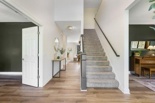 Bright and welcoming foyer features warm wood-look flooring, a carpeted staircase with dark railing, and an open sightline into the main living areas.