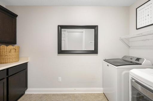 Upper-Level Laundry Room: Dedicated laundry space equipped with washer and dryer, built-in lower cabinets with folding counter space, upper cabinetry, and wire shelving for optimal organization.