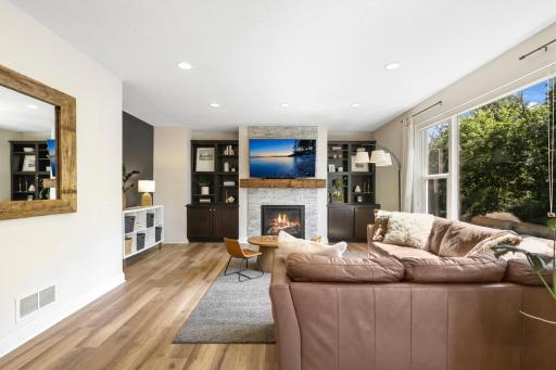 Cozy & Stylish Living Space: Centered around a beautiful stone-surround fireplace, this spacious family room features low-maintenance wood-look flooring, recessed lighting, and large picture windows framing peaceful outdoor greenery.