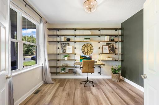 Bright and functional home office showcases custom industrial-style shelving with warm wood shelves. A built-in workspace, and large window create an attractive and productive work-space