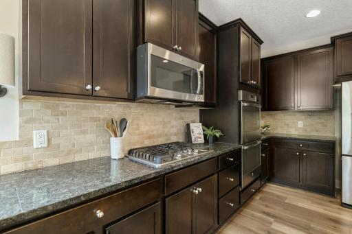 Gourmet kitchen featuring rich espresso cabinetry, granite countertops, and a classic stone tile backsplash. Equipped for culinary enthusiasts with a gas cooktop and sleek stainless steel appliances
