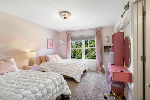 Bright and whimsical upper-level bedroom featuring a custom pastel cloud mural, updated crystal flush-mount light fixture, and a large window overlooking natural greenery.