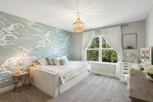 Stylish Guest or Secondary Bedroom: Beautifully appointed bedroom showcasing a feature wall with a wave-patterned wallpaper, a boho beaded chandelier, and large windows with serene outdoor views.