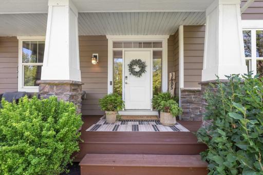 Modern front entry featuring a crisp white door with sidelights, decorative stone-accented columns, exterior lighting, and a spacious porch area creating great curb appeal.