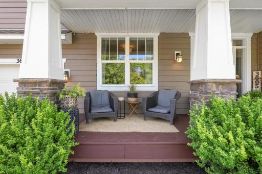 Charming front porch styled with craftsman-inspired stone pillars, warm wood decking, and plenty of space for a cozy outdoor seating area surrounded by lush landscaping.
