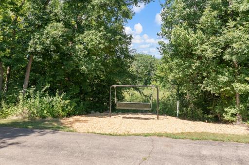 Steps from your doorstep lies the entrance to a picturesque, tree-lined walking path! Complete with a cozy bench swing resting beneath lush canopy trees, this scenic trail meanders through private greenery and connects directly to a park & play areas