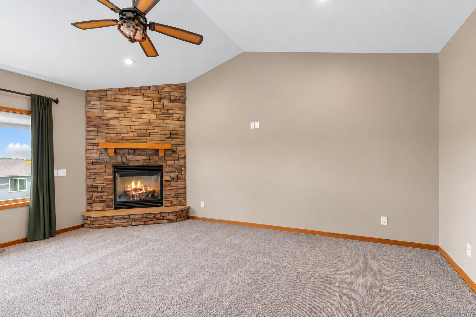 Another view of the great room highlighting the stone fireplace, vaulted ceiling and full-length window treatments
