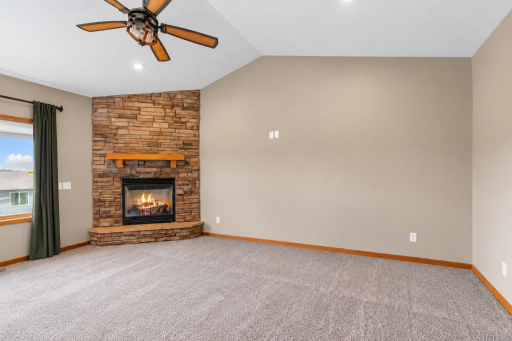 Another view of the great room highlighting the stone fireplace, vaulted ceiling and full-length window treatments