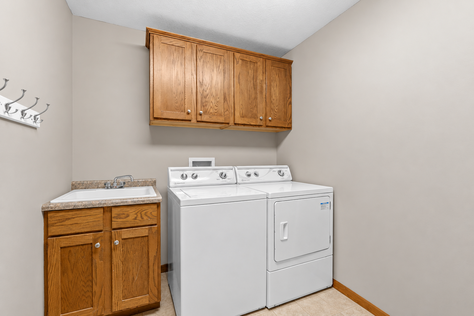Main-level laundry room with utility sink, cabinetry and included washer and dryer