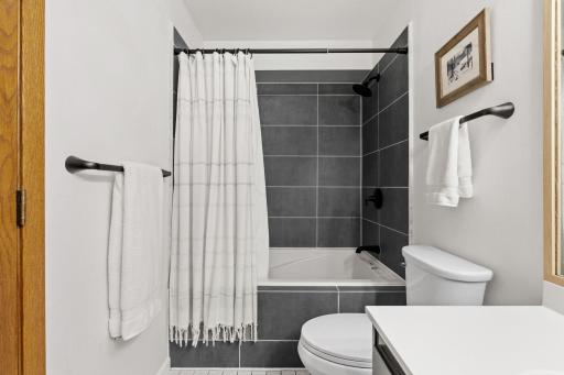 Full bath showing the tub and shower with a tiled surround and matte black fixtures.