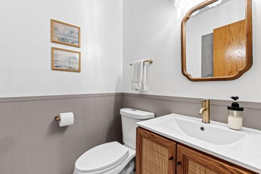 Lower level bath, updated in 2024 with a wood vanity with cane cabinet fronts, wainscoting, and brass fixtures.