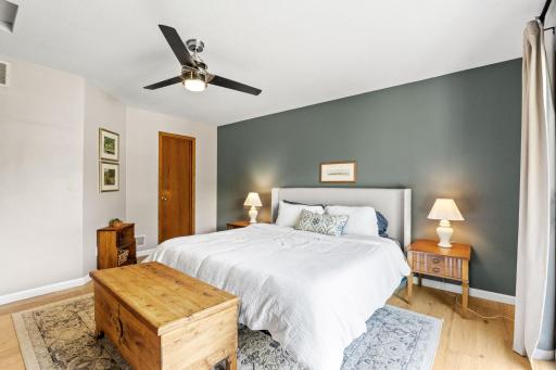 Primary bedroom with a painted accent wall, ceiling fan, and white oak flooring.