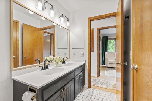Upper level bath with a double vanity, oak framed mirror, sconce lighting, and tile flooring.