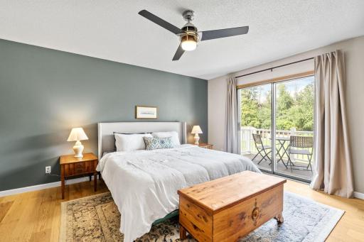 Primary bedroom with a sliding glass door to a private balcony, ceiling fan, and white oak engineered hardwood flooring.