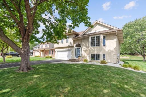 Front exterior framed by a mature shade tree, with an open front lawn and rock edged landscaping beds.