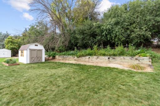 Backyard with a timber retaining wall, planting beds, and a storage shed. Walk through the backyard to grab tea at Season's Market!