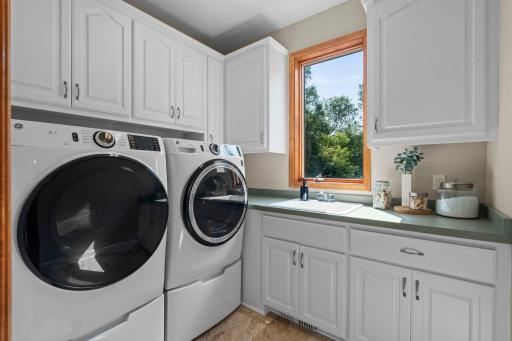 Main level laundry room complete with a sink, stunning cabinetry and a beautiful back yard view.
