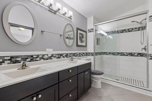 The primary 3/4 bathroom showcases thoughtful updates, including heated tile flooring, a tiled shower with glass door, linen closet. and a double vanity.