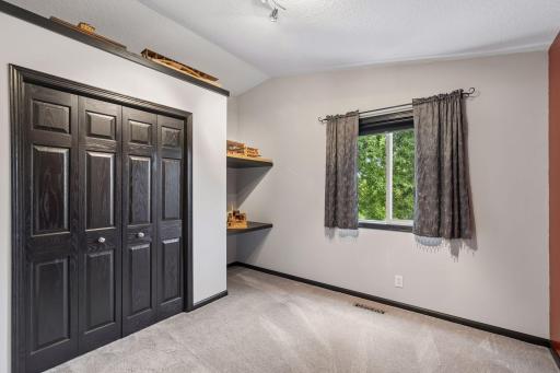 Vaulted ceilings enhance the second upper level bedroom, complemented by carpet flooring, a double window, overhead track lighting, built-in shelving and a double closet.