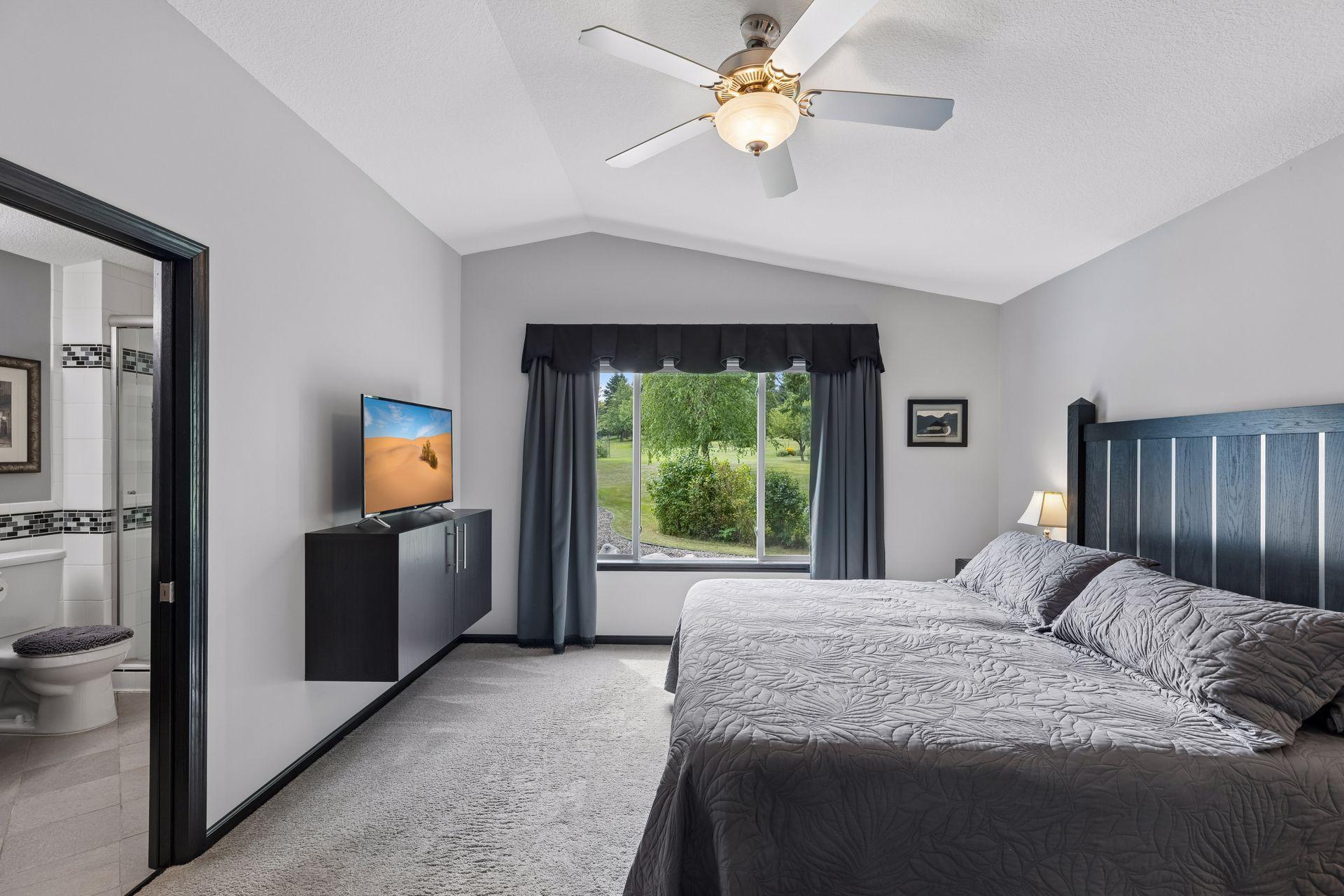 Vaulted ceilings enhance the upper level primary bedroom, complemented by carpeted flooring, a large window, ceiling fan with light, and a walk-in closet with custom built-in storage.