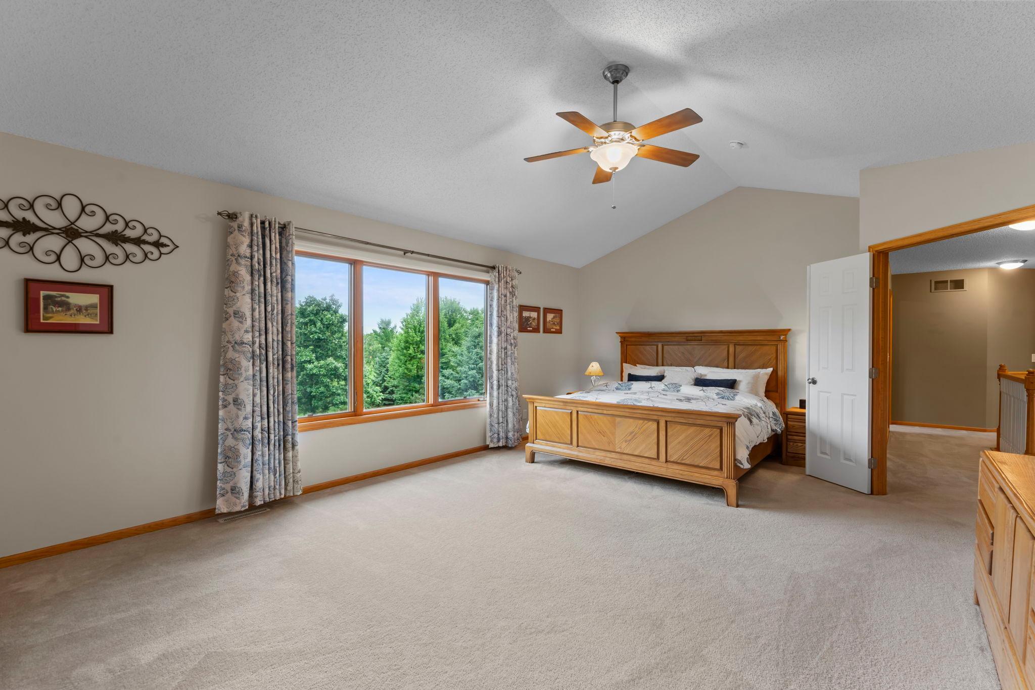 Primary suite through french doors offers a large window with backyard views and vaulted ceilings