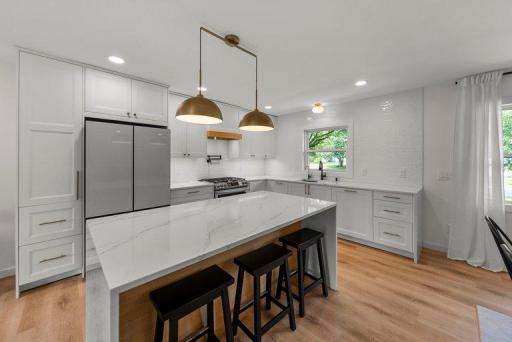 Beautifully remodeled kitchen featuring quartz countertops, custom cabinetry, a stylish tiled backsplash, and premium Samsung Bespoke white glass appliances, including a gas range and refrigerator.