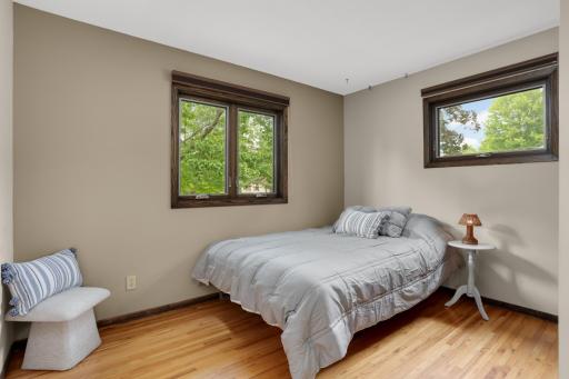 A bright second bedroom with wood floors and two windows offering views of the mature surroundings.