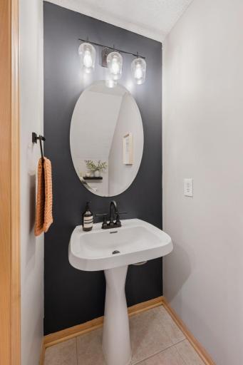 Stylish main-level half bath featuring a pedestal sink, round mirror, modern lighting, and accent wall.