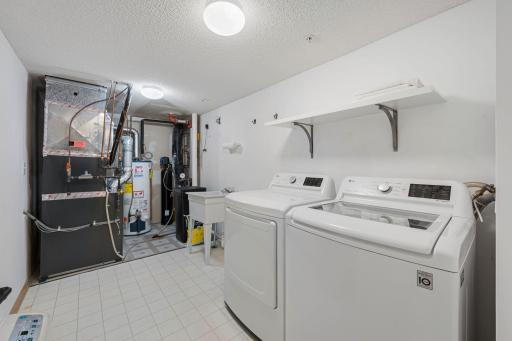 Spacious laundry and utility room with washer, dryer, utility sink, shelving, and additional storage space.