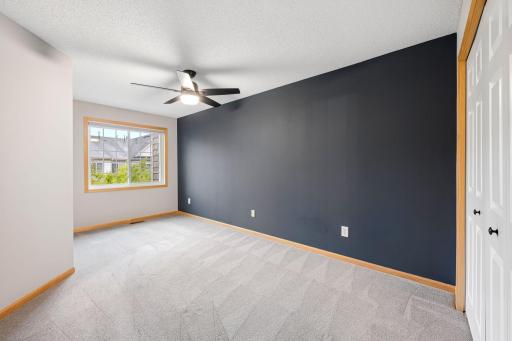 Spacious second bedroom with fresh carpet, ceiling fan, large window, and stylish accent wall.
