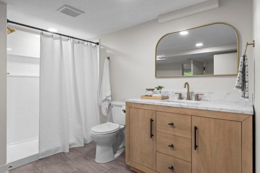 Adjacent to the bedroom is a walk-through bathroom featuring a tiled walk-in shower, vanity, and built-in shelving for added organization. The lower level also includes laundry hookups and a new utility sink.