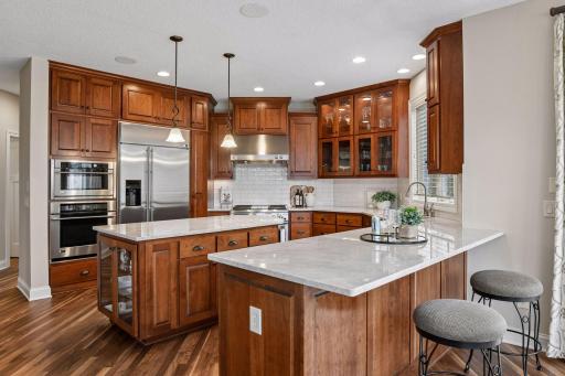A chef-inspired kitchen with quartzite countertops, abundant cabinetry, glass-front display cabinets, and expansive work surfaces.