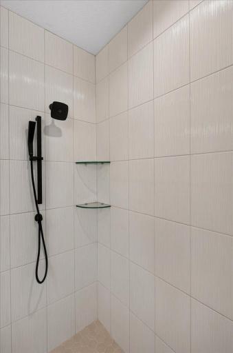 Tiled walk-in shower with shower head and hand sprayer.