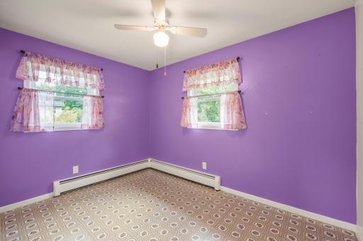 Bright corner bedroom with two windows, a ceiling fan, and baseboard heat.