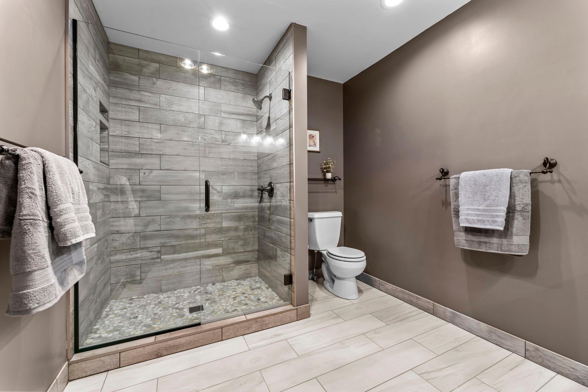 Private ensuite bath complete with a spacious tiled walk-in shower and a custom glass shower door (2024).