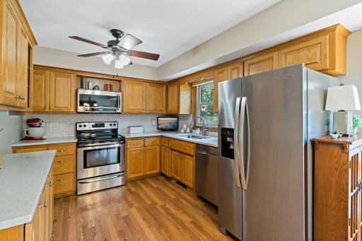 The kitchen features abundant natural wood cabinetry, generous counter space with quartz countertops, stainless steel appliances and a classic subway tile backsplash. A window above the sink brings natural light into the workspace.