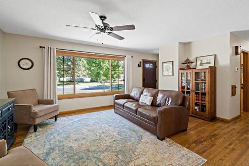 The front entrance opens into a bright, spacious living room where a large picture window fills the space with natural light. Warm hardwood floors and wood accents add character and warmth.