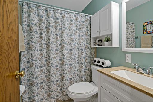 The main-level full bathroom features a tub and shower combination, updated vanity with generous counter space, built-in storage and a fresh, inviting color palette.