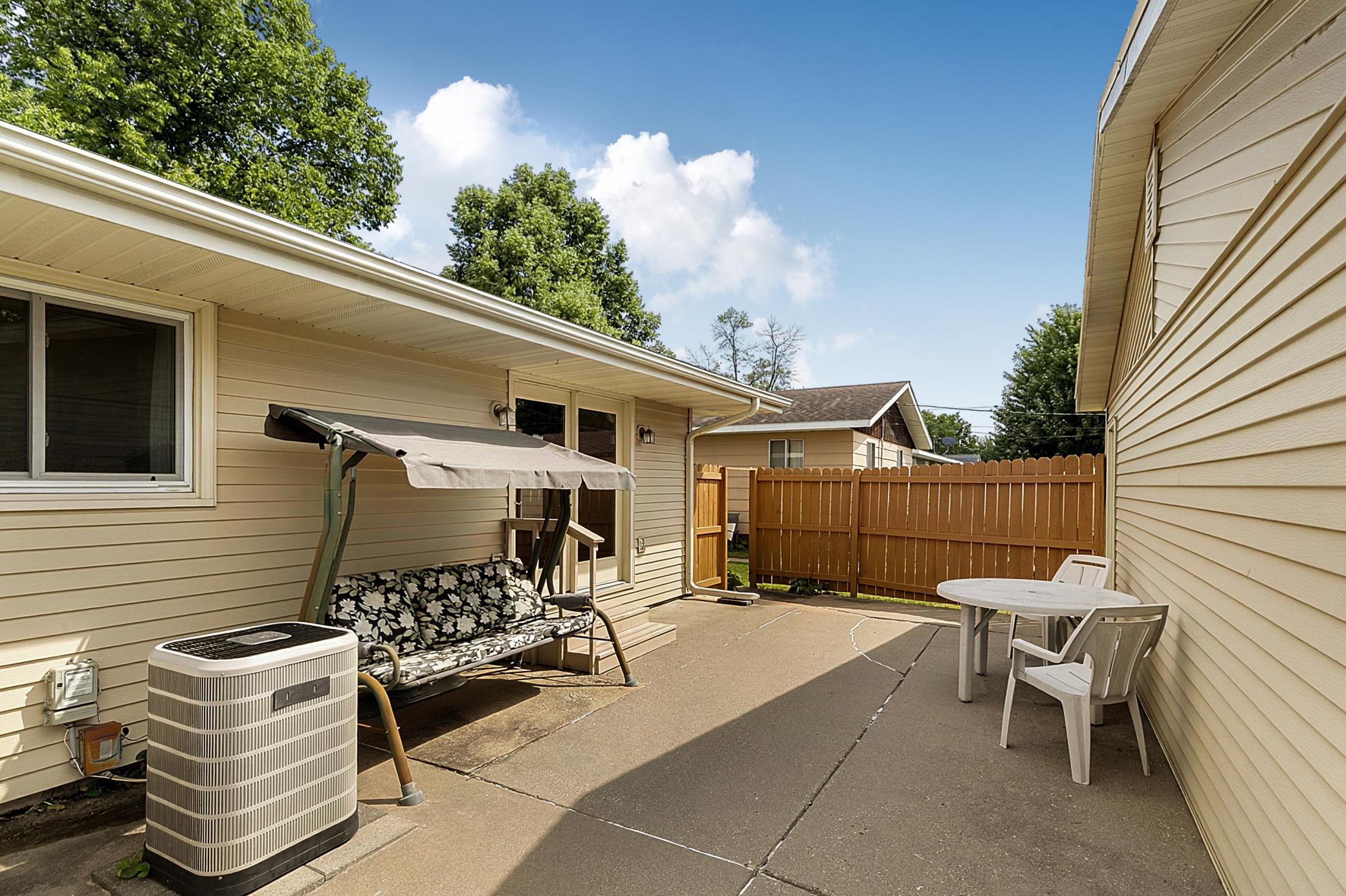 Spacious concrete patio between house and detached garage with a partial wood fence for privacy that has recently been painted.