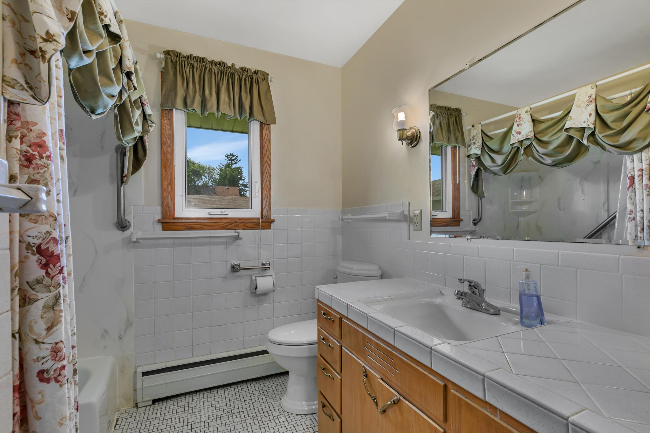 The main level three-quarter bathroom with tiled vanity, tiled backsplash and a tub that’s been notched/cut out for a walk in tub/shower. There is also a double linen cabinet and a newer exhaust fan that’s roughly 2 years old.