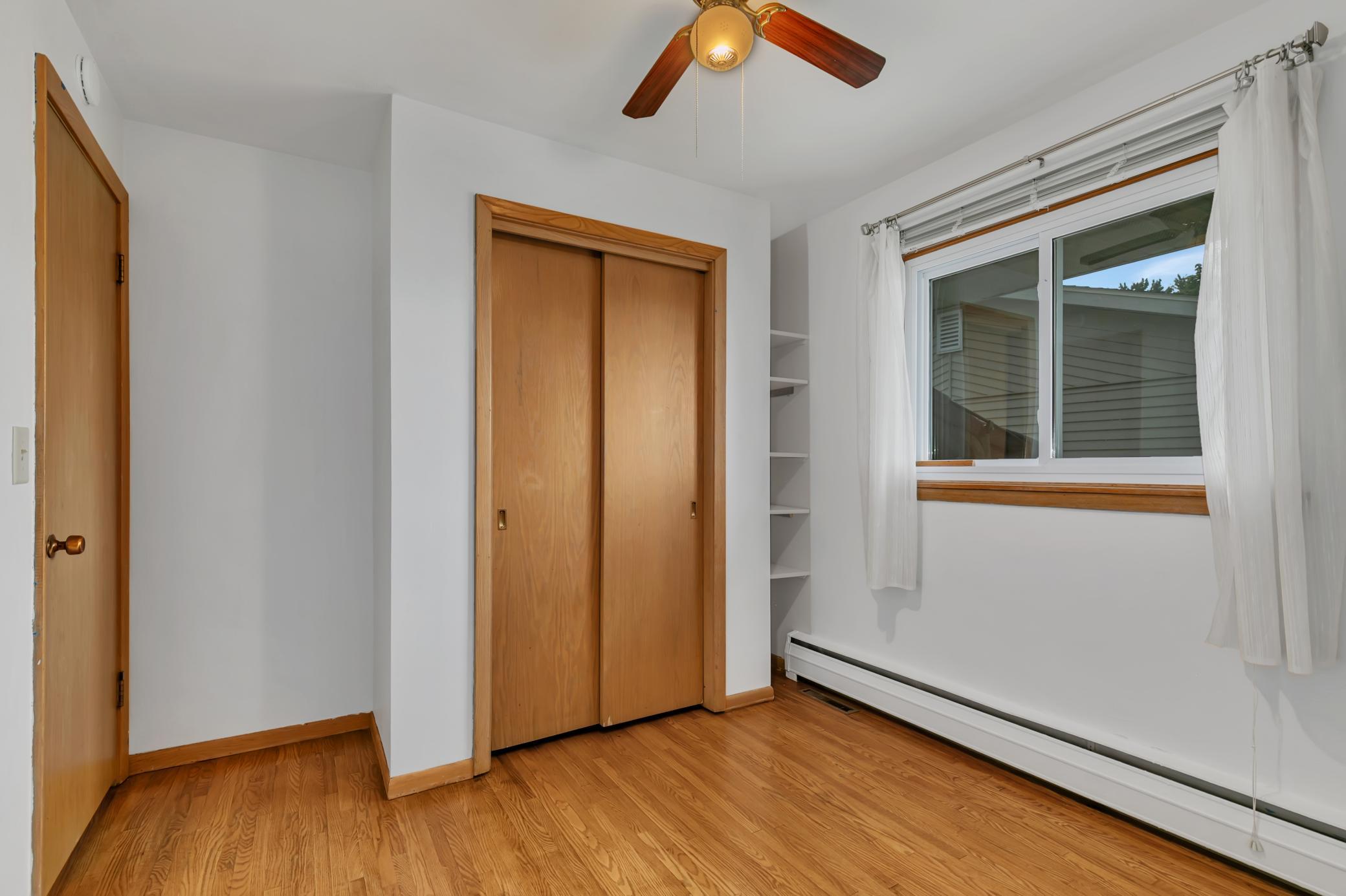 Third main level bedroom with a small nook with shelving, a ceiling fan and hardwood floors.