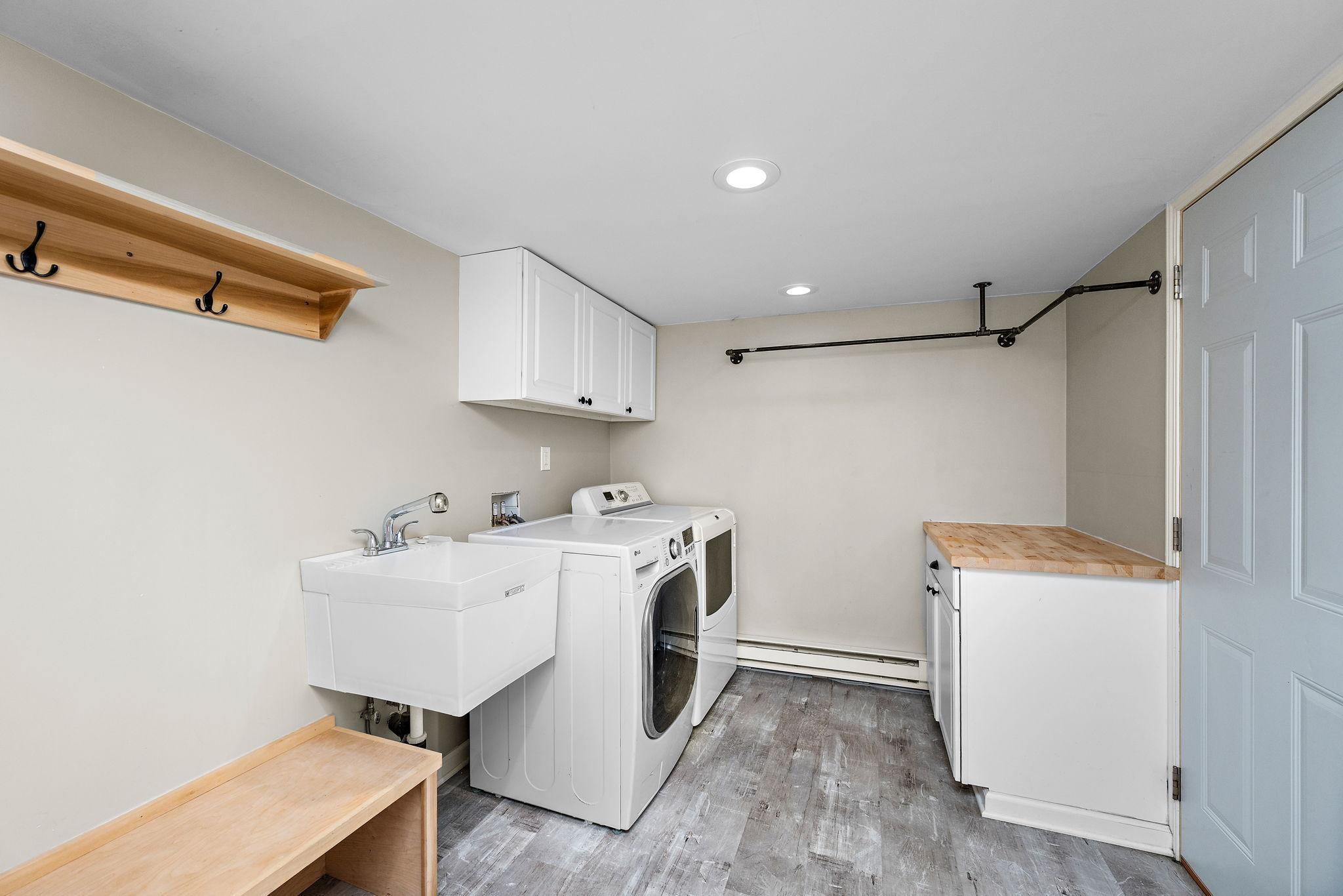 Super rare mudroom / main floor laundry with coat and shoes storage, cabinet and counter space, hanger bars, supplemental heat, and a sink… it checks all the boxes!